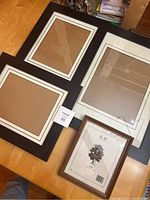 Set of four certificate frames laid out on wooden floor, showing various sizes and style with dark border and white matting.