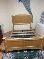 Front view of pine double bed frame showing headboard and footboard in a room with hardwood floor and rug underneath.