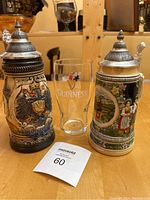 Photo showing both German and Swiss steins with Guinness glass in between on a wooden table, highlighting the size and design details of all three items.
