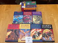 Full set of seven Harry Potter hardcover books with dust jackets arranged in two rows on a wooden table with the box behind.