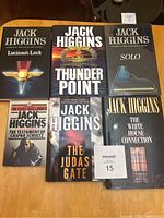 Top view of six Jack Higgins books including five hardcovers and one softcover arranged on a wooden surface, showcasing titles and cover art.