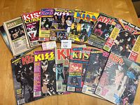 Wide shot showing 15+ KISS magazines from late 1970s/early 1980s with visible wear and some missing covers or pages.