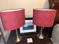 Photo showing both red patterned lamps and framed iceberg photo on a wooden night stand.