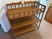 Front and angled view of solid oak baby change table showing top platform with railing and two lower open shelves
