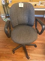 Front view of gray fabric office chair showing padded seat and backrest with black armrests and caster wheel base.