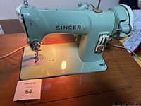 Close-up of Singer sewing machine showing light green color, brand name, sewing needle area, and working light on.