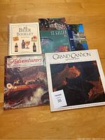 Photo of all five books laid out on a wooden floor, showing titles and covers of each book including the Beer Booklet, St. Gallen, Herrschaftsweg, Adventurers, and Grand Canyon National Park.