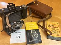 Kodak Vigilant Six-20 camera with folded bellows extended, instruction booklet, Kodaguide booklet, and brown leather carrying case with strap shown on wooden surface.
