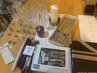 Full lot showing champagne flutes, the cooler, cake serving set box, wine opener box, pillar candles, taper candles, some wine coasters, and place card holders.