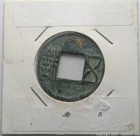 Front side of the Wu Zhu coin showing Chinese characters and the square hole, held in a white cardboard holder with staples.