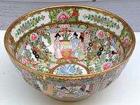 Side angle view showing the bowl's interior with colorful Manchu figures and floral decoration, gold rim visible.