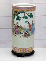 Full view of Famille Rose ceramic umbrella stand on dark wooden base, showing detailed painted figures and floral borders on cylindrical ceramic body.