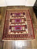 Full view of carpet laid out on wooden floor showing three geometric patterns and outer borders in red, purple, cream, and brown.