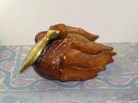 Front-side view showing wood body and brass beak of pelican sculpture.