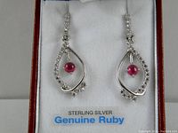 Pair of sterling silver earrings with genuine ruby stones and cubic zirconium accents displayed in a white cushioned box.