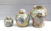 Wide shot of three porcelain pieces: one large vase and two lidded jars all decorated with Famille Rose patterns and Chinese figures.