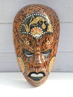 Front view of brown wooden tribal mask with black, gold, and red painted designs and carved geometric texture.
