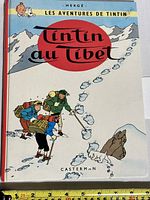 Front cover of the hardback book Les Aventures de Tintin - Tintin au Tibet with characters hiking in snow and large red title circle in the background.