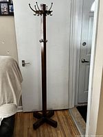 Full view of the antique coat tree stand showing the tall wooden body, cross base, and hooks at the top.