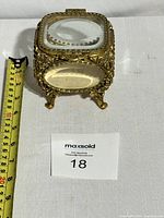 Front view showing ornate filigree metalwork, beveled glass panels, decorative feet, and measuring tape for scale