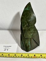 Front view of the green and dark stone sculpture standing next to a measuring tape showing about 9.5 inches height.