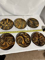 Five vintage circular side plates with distinctive abstract brown and ochre patterns spread in two rows with measuring tape showing size.