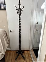Full view of the coat tree stand showing overall height, finial top, hooked ring, twisted column, and base.