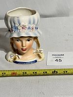 Front view of the vintage Relpo lady head planter showing the face and pigtails with the floral hat.