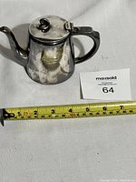 Side view of silver teapot with hinged lid closed, showing tarnish and used condition.