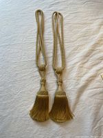 Pair of gold curtain tie backs displayed flat on light fabric background.