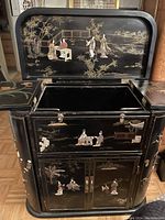 Front view of cabinet with top lid open showing painted interior of lid, side flaps and front panels with carved scenes