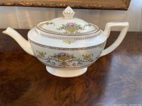 Photo of the front and side view of the antique Mintons Talbot teapot, showing floral decorations and gold detailing.