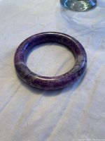 Purple jade bangle resting on a light fabric surface, showing color and texture details
