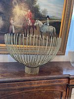 Decorative centerpiece or candleholder with vertical metal rods and circular metal base, shown on a wooden surface.
