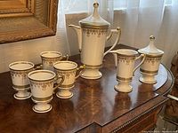 Full view of the coffee pot set with four cups, creamer, and sugar bowl on wood table by mirror and window showing overall condition and design
