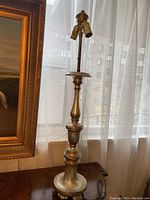 Tall wooden gold leaf lamp shown next to window and framed painting, visible gold leaf finish with minor base chips and new twin sockets.