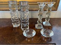 Set of four crystal candlesticks and two round crystal bowls displayed on a wooden surface in front of a framed painting.