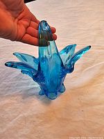 Photo showing side view of blue Murano glass vase with hand holding it to show scale and its petal-like points curving outward.