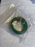 Pair of small green jade bracelets inside clear plastic bag on white fabric background.