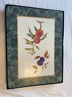 Close-up photo of a Royal Worcester Evesham pattern placemat with fruit branches artwork, oranges and plums, on a green patterned background.