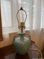 Photo of a vintage MCM blue pottery lamp with ceramic base and brass light fixture, showing the front and part of the curved side handles.