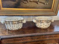 Both cache pots displayed side by side on a wooden surface beneath framed art