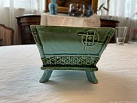 Front view of vintage small two-tone green ceramic planter with lattice detail and knot design, showing all four legs and the shape of the planter.