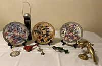 Three collectible bird plates with floral and bird designs displayed on stands, plus various bird-themed items including a suet feeder and small figurines