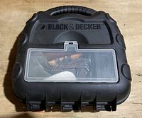 Closed black hard plastic carrying case with handle showing Black & Decker branding and transparent window with Mouse logo visible inside.