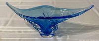 Blue transparent glass decorative bowl with extended wavy edges and solid sculpted base placed on a striped fabric.