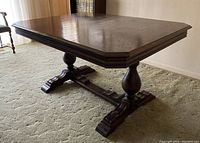 Wood dining table with the leaf attached, increasing the table top length to 64 inches. The table has a dark polished finish and detailed carved base.