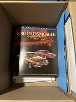 Box containing 1980 Oldsmobile brochure on top, showcasing car models in good condition