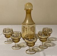 Full set showing the decanter and five matching glasses arranged on white cloth.