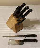 Photo showing Henckels cutting utensils arranged with knives in wooden block and two knives lying in front on a table.